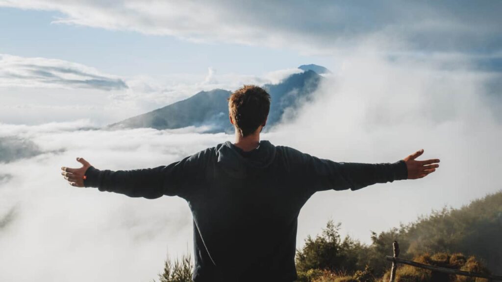 Photo of a man with his arms stretched wide at the top of a mountain