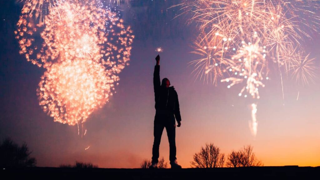 Photo of a person raising their hand with fireworks in the back